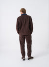 A male model is wearing the Cacao Cord Utility Jacket shown from a back angled perspective against a plain studio background, emphasizing the fit, tailored shoulders, and rich cacao brown corduroy texture.