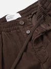 A close-up detail photo of the Cacao Cord Pleated Track Pant set on a plain white background. The shot focuses on the adjustable drawstring waist, front pleat stitching, and fine corduroy cotton texture.