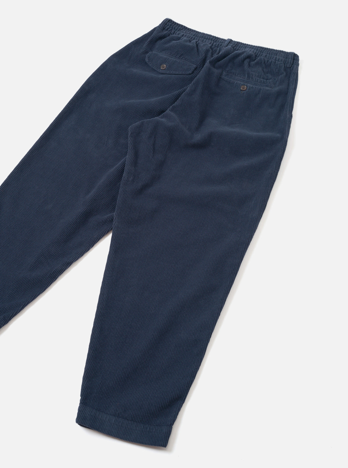 A rear view of the Dark Navy Cord Pleated Track Pant displayed flat on a clean white background, showcasing the back pockets, flexible waistband construction, and deep navy blue corduroy fabric finish.