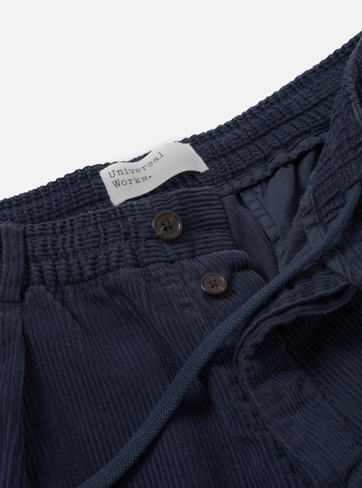 A close-up image showing the waistband and front pleats of the Dark Navy Cord Pleated Track Pant against a white studio background, detailing the dark corduroy texture and drawcord waist closure.