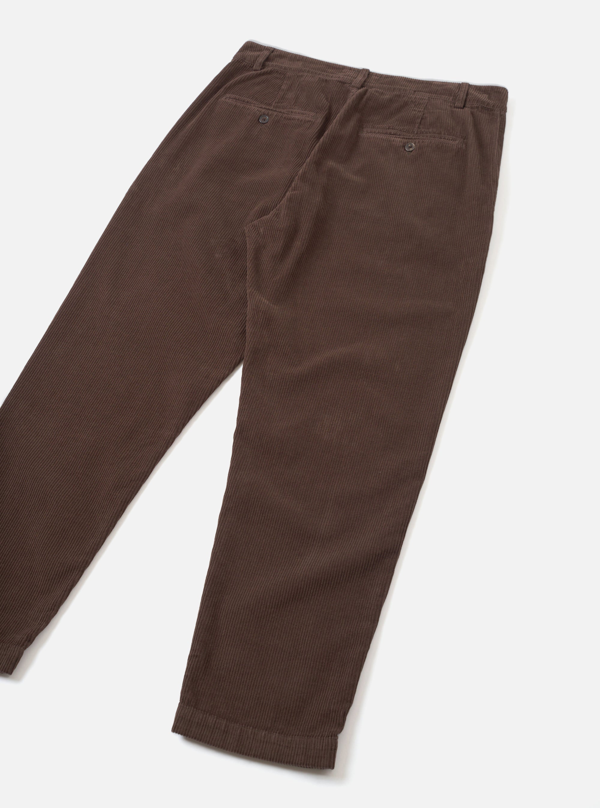 Flat lay of cacao brown corduroy military chinos on a light grey background, showing the back. Fine-wale cord texture visible throughout. Two buttoned welt back pockets, a belt loop waistband, and turned-up cuffs at the ankle. Trousers taper toward the hem.