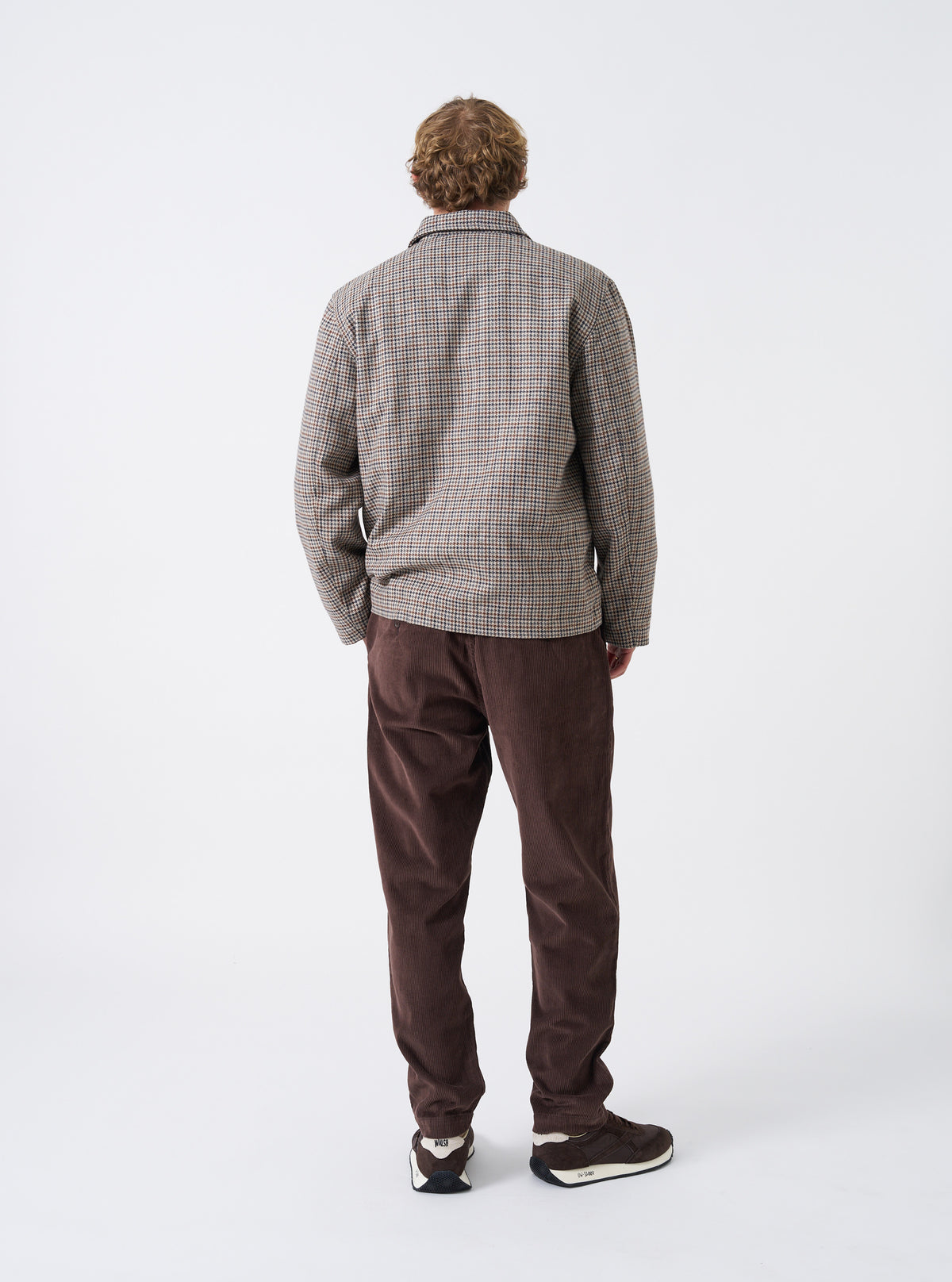 A male model is wearing the Cacao Cord Military Chino shown from a side and rear angle against a plain light background, highlighting the rear pocket placement, slim straight fit, and corduroy material.