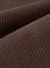 Close-up detail shot of cacao brown corduroy fabric, showing wide, clearly defined wales running diagonally across the frame. The raised ridges and textured valleys of the cord are sharply in focus, highlighting the soft, dense pile and matte finish of the material.