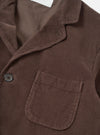 Side profile view of the Cacao Cord Three Button Jacket worn by a model against a plain studio background. The shot highlights the fit through the sleeve, soft unstructured shoulder line, and rich cacao brown corduroy fabric.