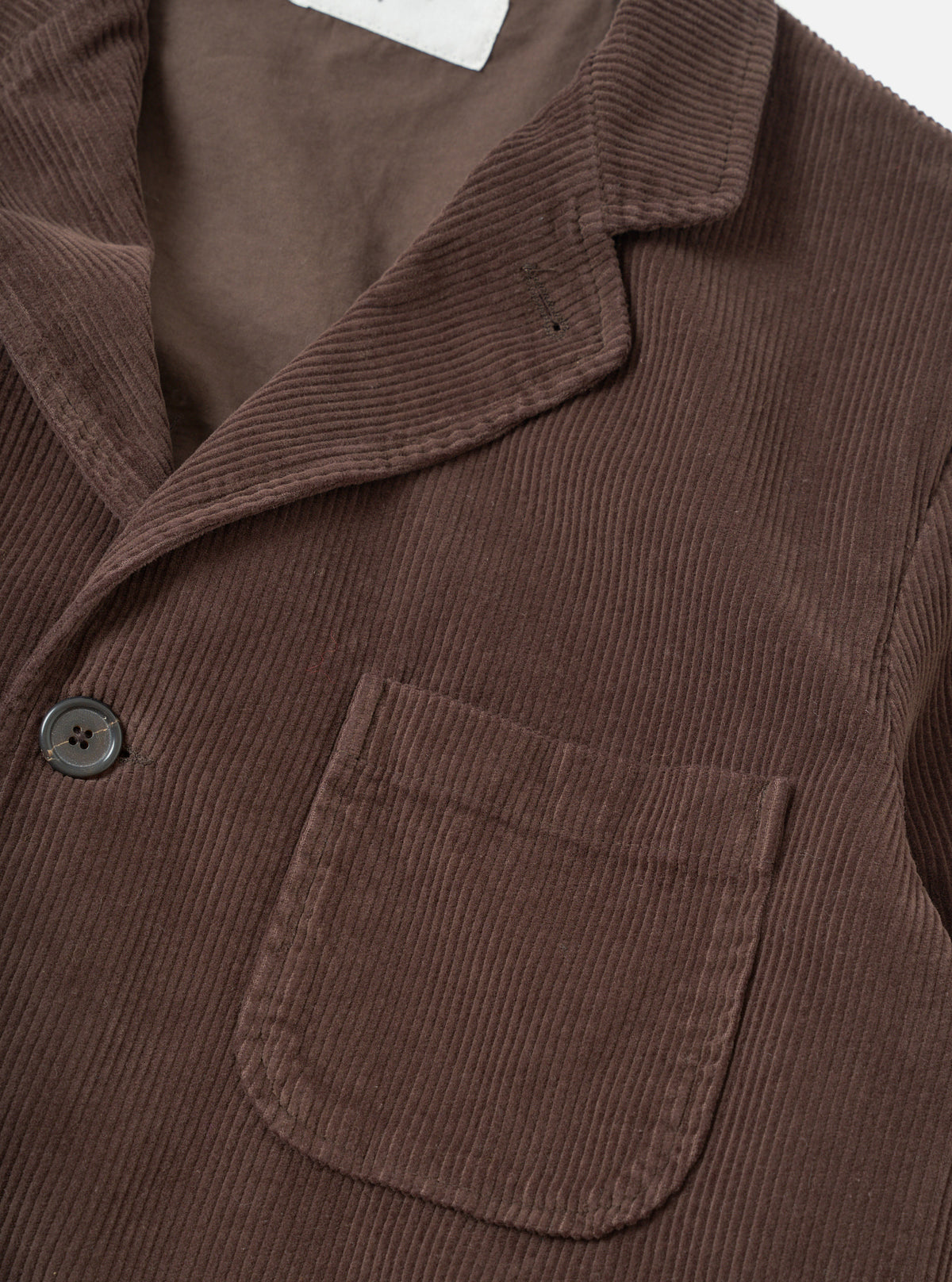 Side profile view of the Cacao Cord Three Button Jacket worn by a model against a plain studio background. The shot highlights the fit through the sleeve, soft unstructured shoulder line, and rich cacao brown corduroy fabric.