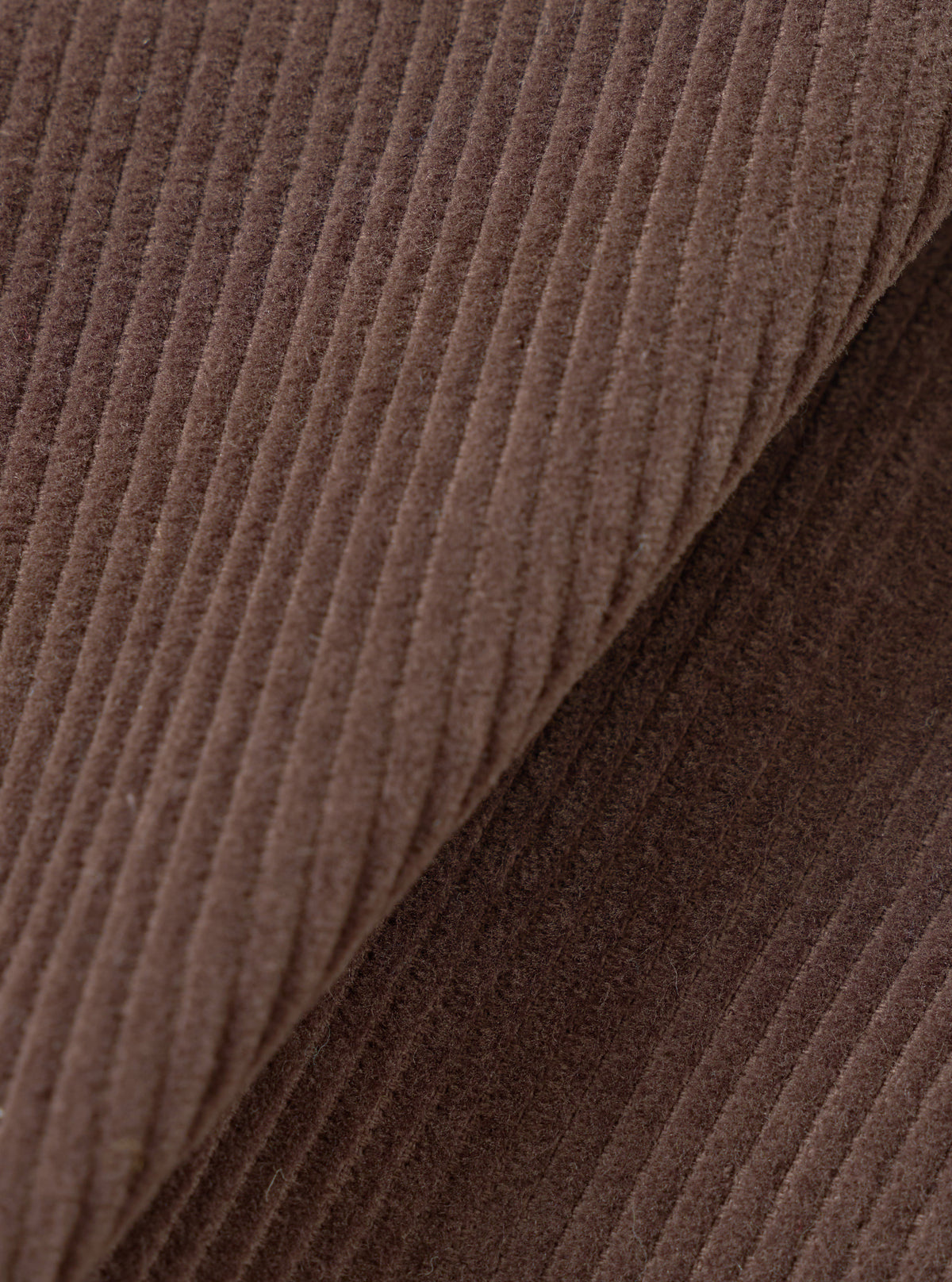 Extreme close-up fabric swatch of the Cacao Cord Three Button Jacket, fill-frame shot against a plain background. The detail showcases the ribbed wale texture, soft velvet finish, and deep brown hue of the pure cotton corduroy.