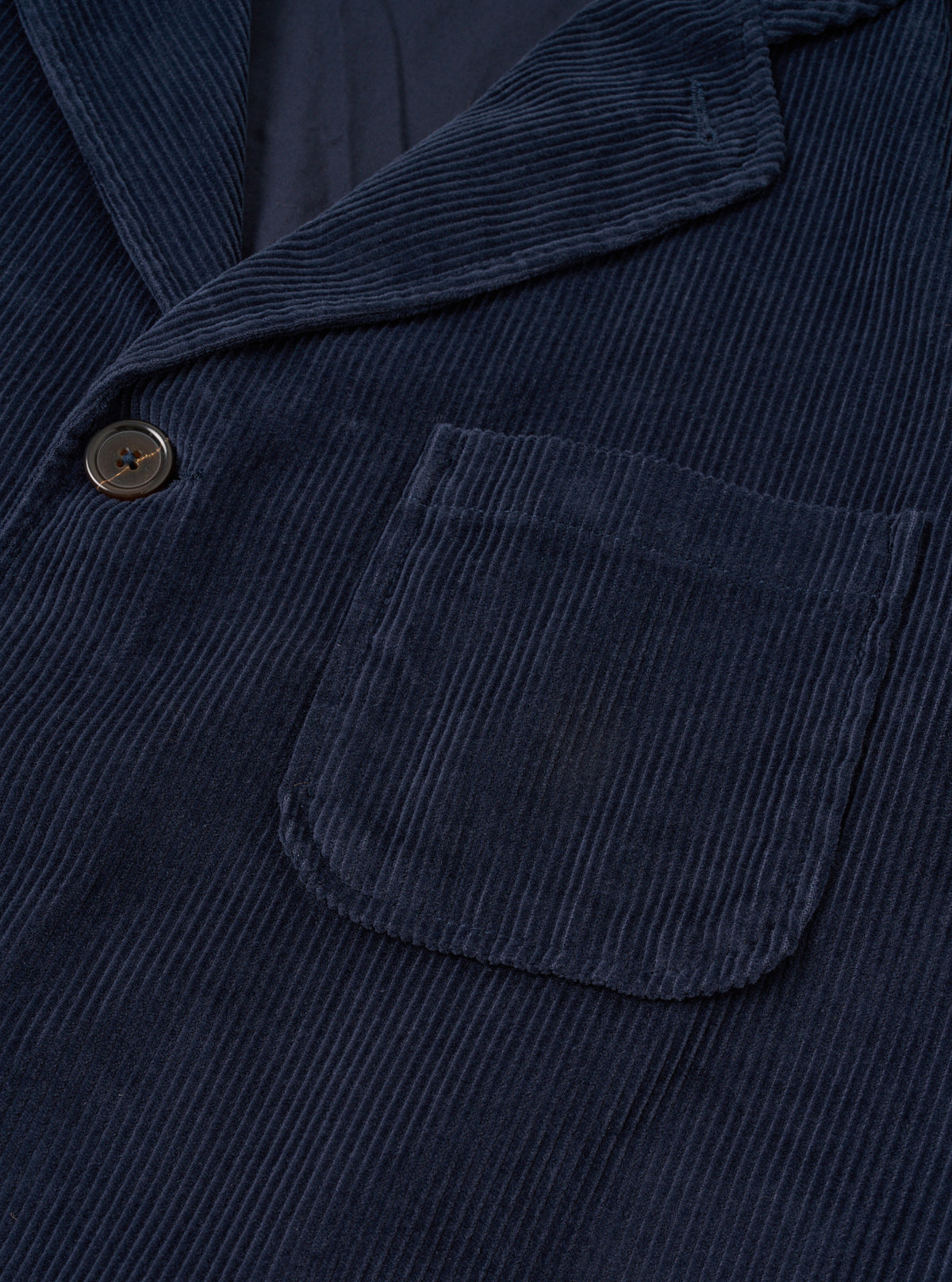 Angled side view of the Dark Navy Cord Three Button Jacket worn by a model against a clean studio background, showing the relaxed fit, sleeve length, notch lapel collar detail, and fine dark navy corduroy texture.