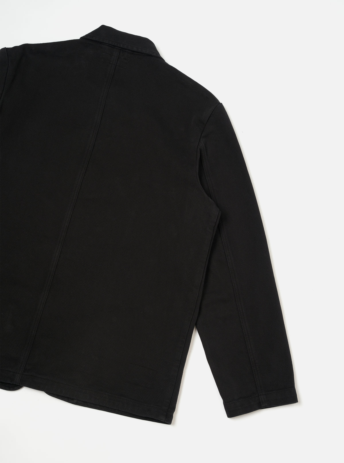 Back view of the Black Dexter Twill OG Bakers Chore Jacket displayed flat against a plain off-white background. The shot highlights the clean back paneling, shoulder seams, and durable black organic cotton twill construction.