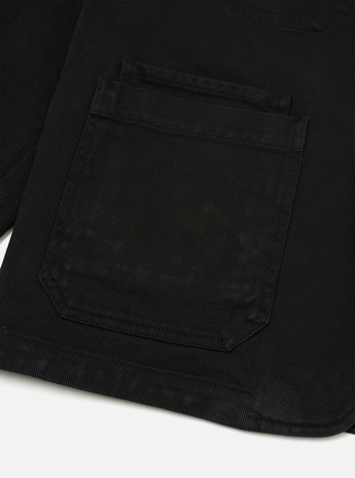Side view of the Black Dexter Twill OG Bakers Chore Jacket presented against a clean white background. This angle highlights the classic sleeve construction, side seams, and structured fit of the black organic cotton twill fabric.