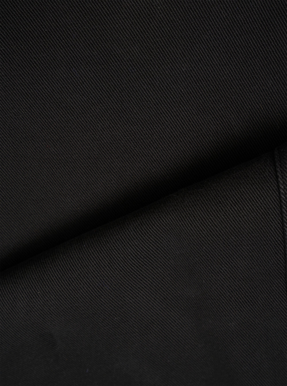 A close-up fabric swatch view showing the fine weave and detailed surface texture of the organic cotton twill used in the Black Dexter Twill OG Bakers Chore Jacket. The frame is filled entirely with the black fabric.