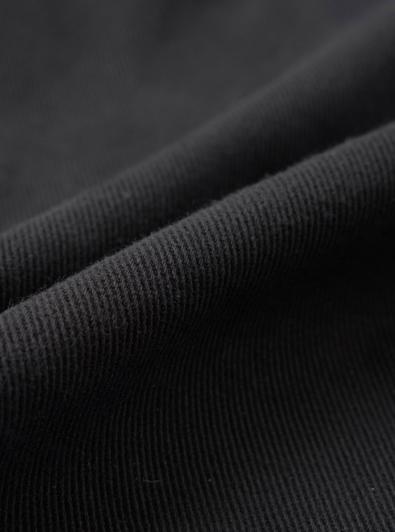 A close-up fabric swatch view displaying the rich texture and fine weave of the organic cotton twill fabric from the Black Dexter Twill Grad Chino. The frame is filled entirely with dark black twill fabric detail.
