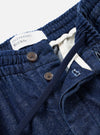 Detailed view of the Indigo Future Denim Oxford Pant against a white background, highlighting the elasticated drawstring waist, single front pleating, and subtle neps in the recycled cotton denim weave.