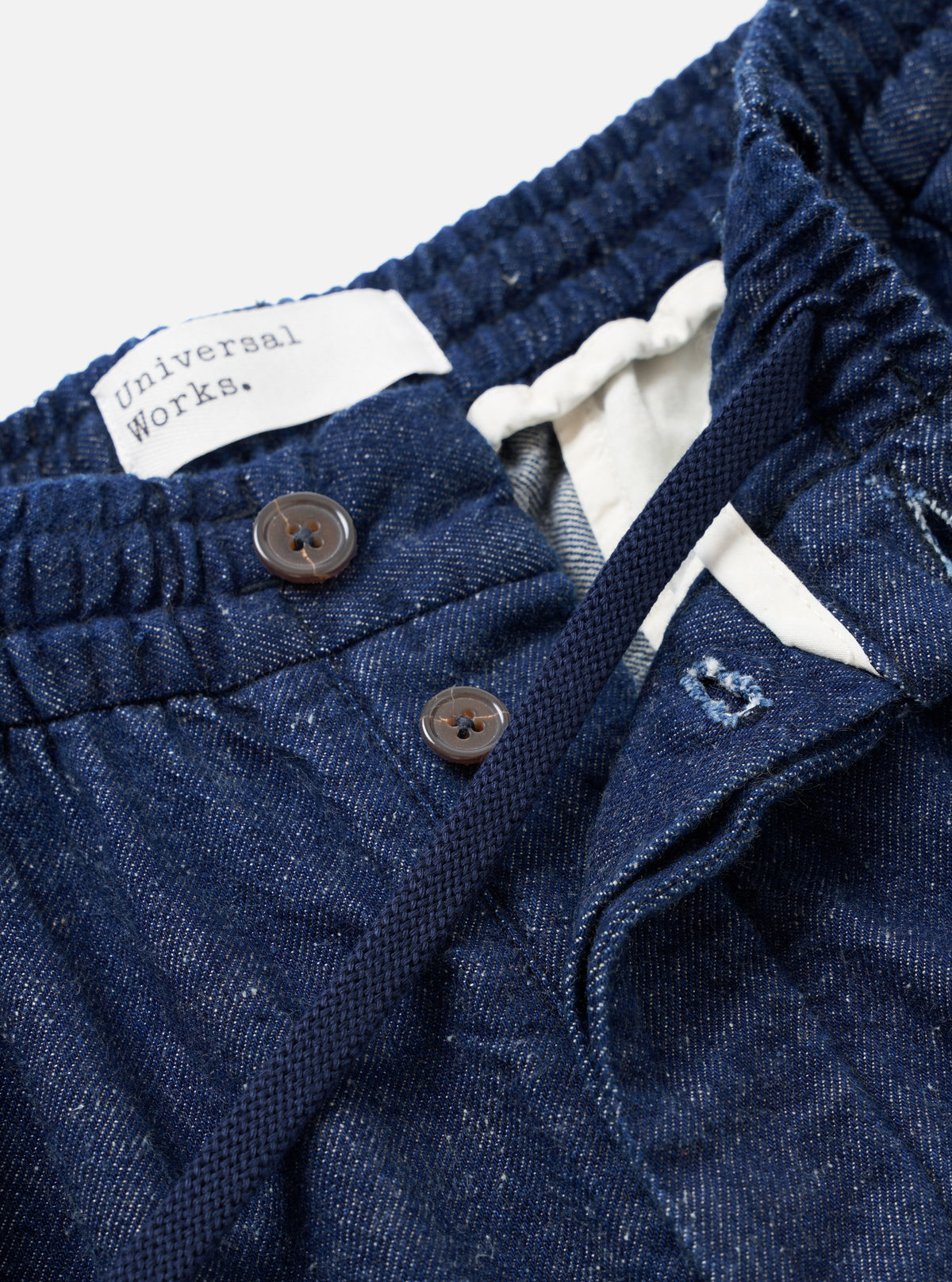 Detailed view of the Indigo Future Denim Oxford Pant against a white background, highlighting the elasticated drawstring waist, single front pleating, and subtle neps in the recycled cotton denim weave.