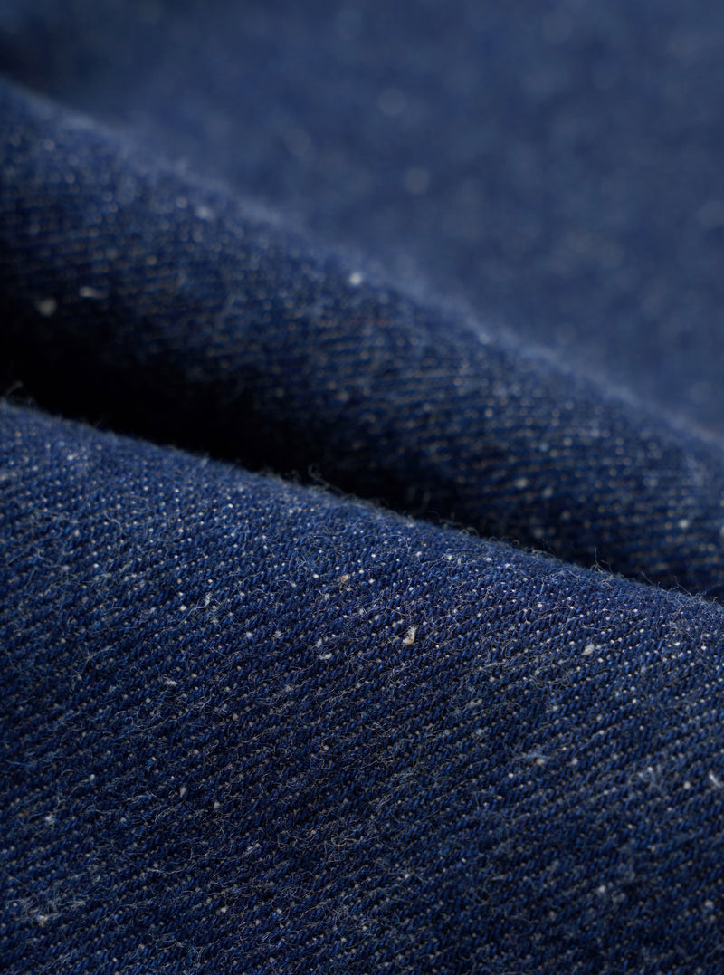 A close-up fabric swatch image capturing the deep indigo shade and textured neps of the organic and recycled cotton denim material used on the Indigo Future Denim Grad Chino. The frame is filled with denim.