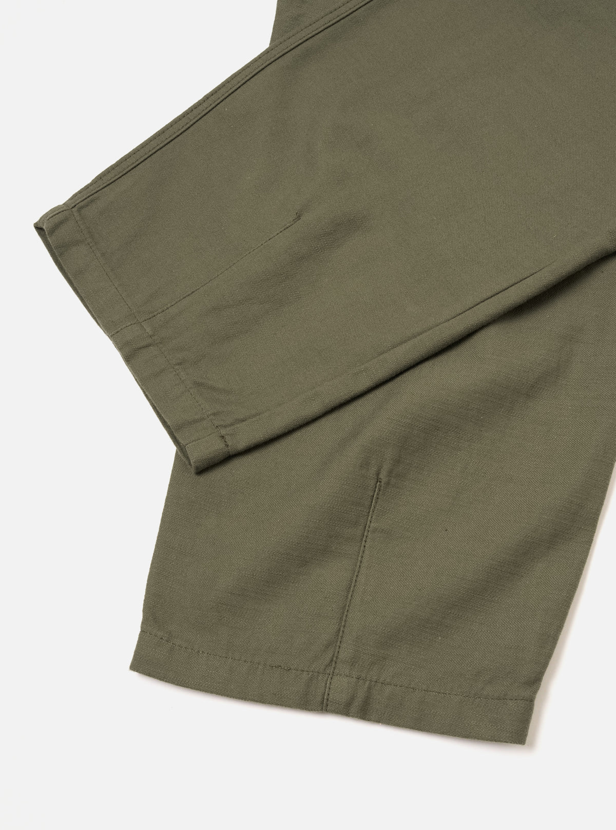 Close-up view of the Olive Slub Sateen Utility Pant on a plain off-white studio background. The shot emphasizes the texture of the slub sateen cotton fabric, waistband construction, belt loops, and stitching.
