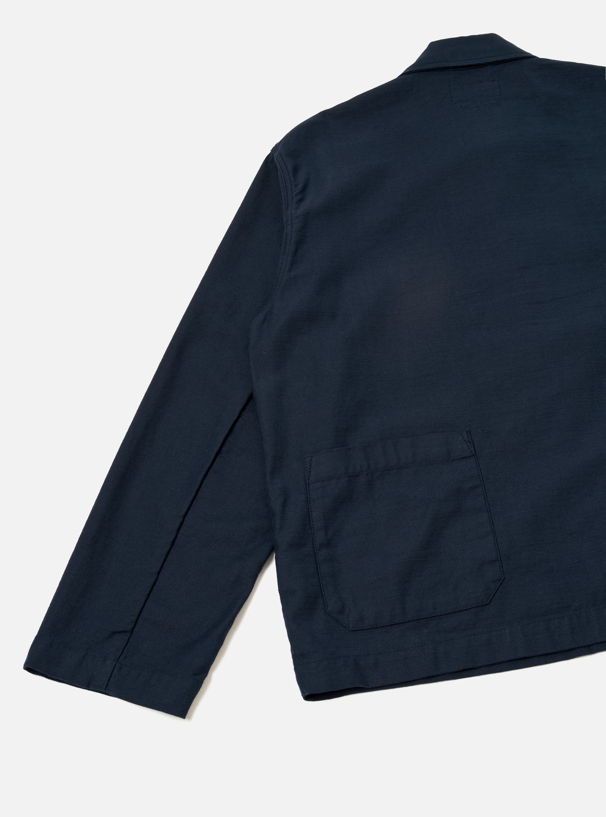 Rear view of the Navy Slub Sateen Ives Jacket set against a clean off-white background. The image highlights the clean straight hemline, structured shoulders, and single rear patch pocket on the lower right back.