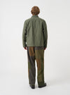 A male model wears the Olive Slub Sateen Ives Jacket, captured in a three-quarter side pose against a plain light grey studio backdrop, highlighting the sleeve length, boxy cut, and side profile view.