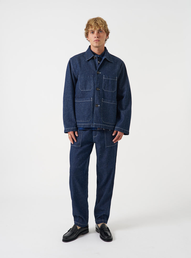 A male model wears the Indigo Future Denim Ives Jacket over a neutral top, standing against a plain light grey backdrop. The full-length shot highlights the relaxed boxy silhouette and indigo denim finish.