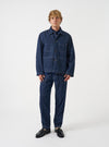 A male model wears the Indigo Future Denim Ives Jacket over a neutral top, standing against a plain light grey backdrop. The full-length shot highlights the relaxed boxy silhouette and indigo denim finish.