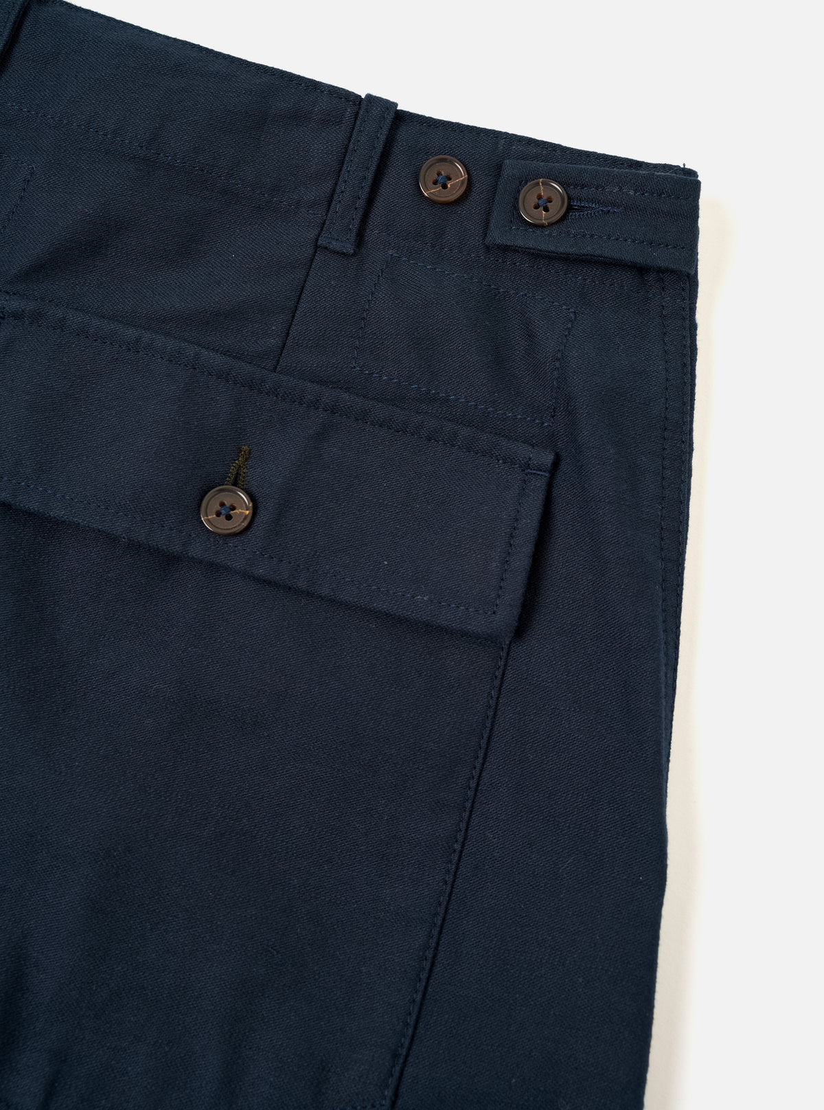 Angled studio shot of the Navy Slub Sateen Loose Fatigue Pant on a neutral off-white background. The composition emphasizes the distinct slub sateen cotton weave, side pocket entry, precise stitching details, and classic utility trouser style.