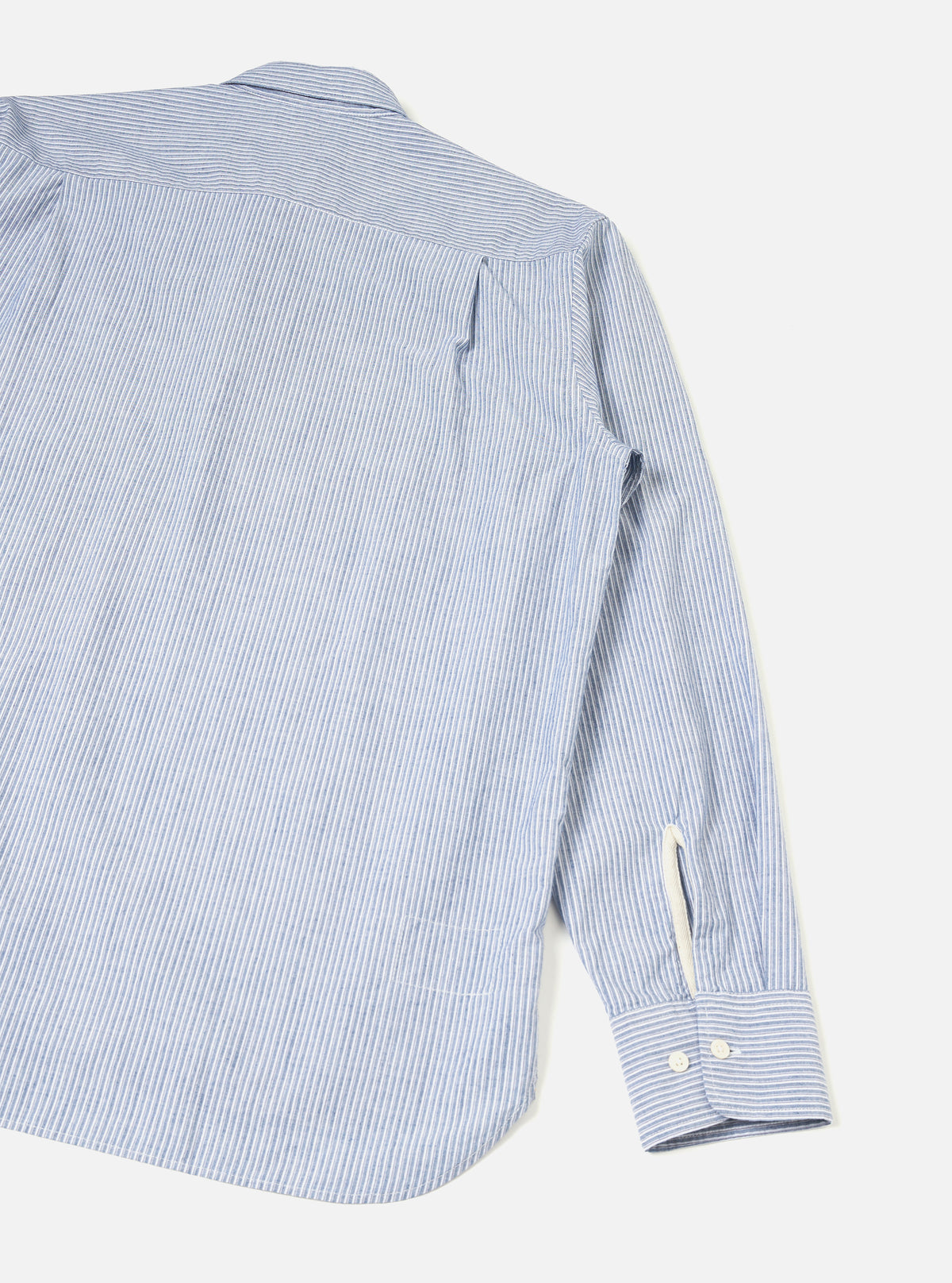 Rear view of the Blue Montgomery Stripe Station Shirt displayed on a clean neutral background. The photograph showcases the vertical blue striped cotton fabric, straight hemline, neat shoulder yoke, and back pleat construction of the garment.