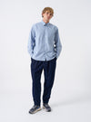 A male model wears the Blue Montgomery Stripe Station Shirt buttoned up, posing against a neutral studio backdrop. The full-length shot illustrates the blue vertical stripe pattern, classic collar, chest pockets, and comfortable relaxed fit.