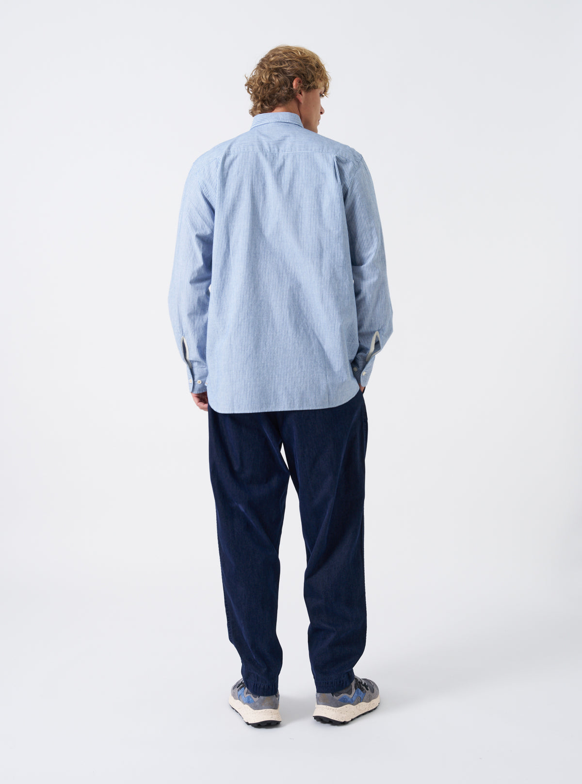 A male model wears the Blue Montgomery Stripe Station Shirt unbuttoned over a plain tee, captured in a three-quarter pose against a plain off-white backdrop. The image shows the blue striped pattern, open front styling, and overall drop.