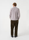 A male model wears the Brown Queens Cotton Patched Shirt posed against a plain studio background. This shot showcases the relaxed fit, woven stripe texture, and distinct patched design from a side angle.