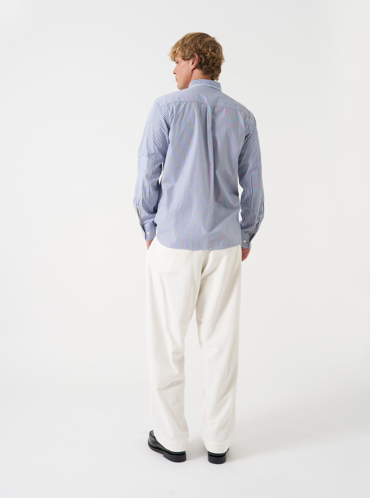 A male model wears the Navy Queens Cotton Patched Shirt styled casually against a neutral backdrop. Captured in a three-quarter pose, the shot showcases the relaxed silhouette and contrasting stripe placements.