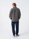 A male model wears the Mid Brown Dam Marl Work Shirt in a back view shot against a plain studio background. The image details the fine marl knit texture, rear shoulder yoke, and hem construction.