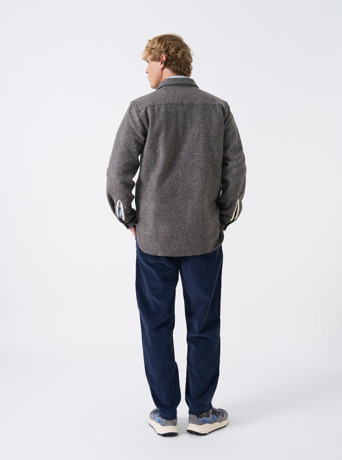 A male model wears the Mid Brown Dam Marl Work Shirt in a back view shot against a plain studio background. The image details the fine marl knit texture, rear shoulder yoke, and hem construction.