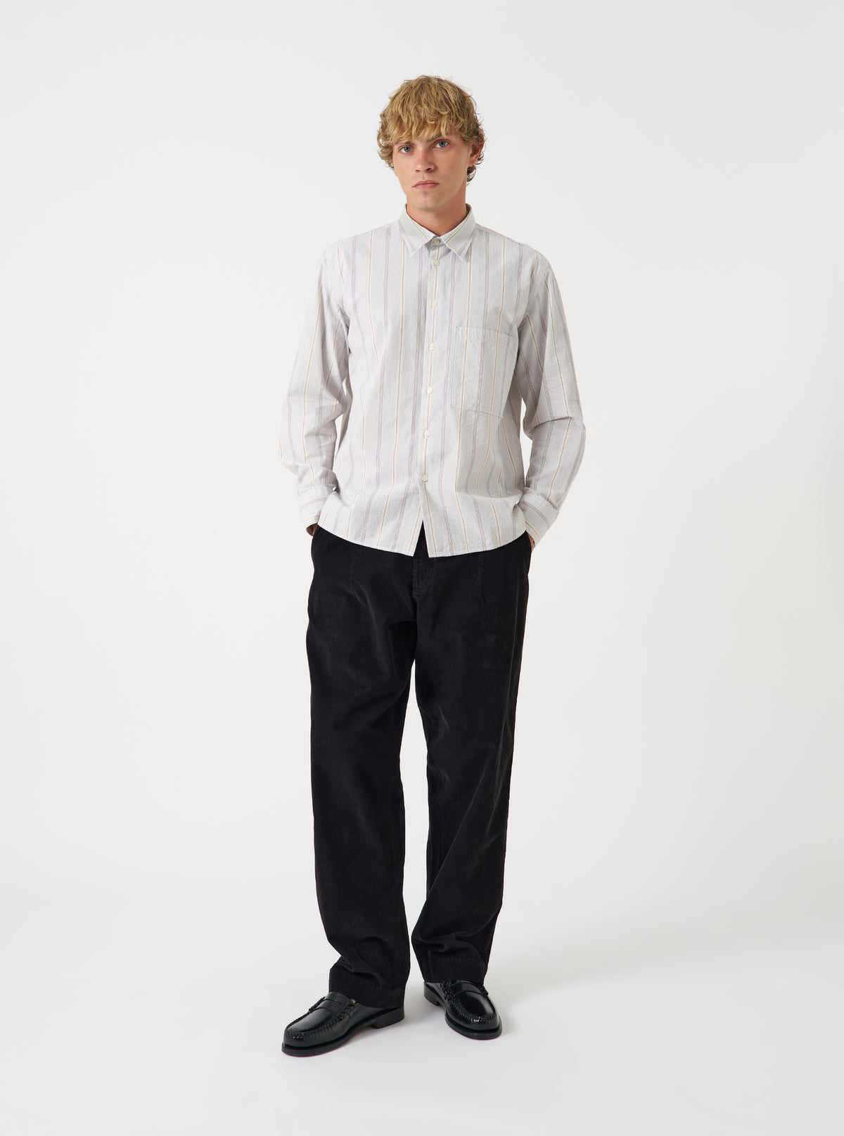 A male model stands wearing the Dove Monk Organic Stripe Square Pocket Shirt against a plain white studio background. The front view highlights the striped pattern, classic button-down front, and fit.
