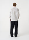 A male model wears the Dove Monk Organic Stripe Square Pocket Shirt in a back view shot against a neutral studio backdrop. The photo details the subtle striped fabric and clean rear silhouette of the shirt.