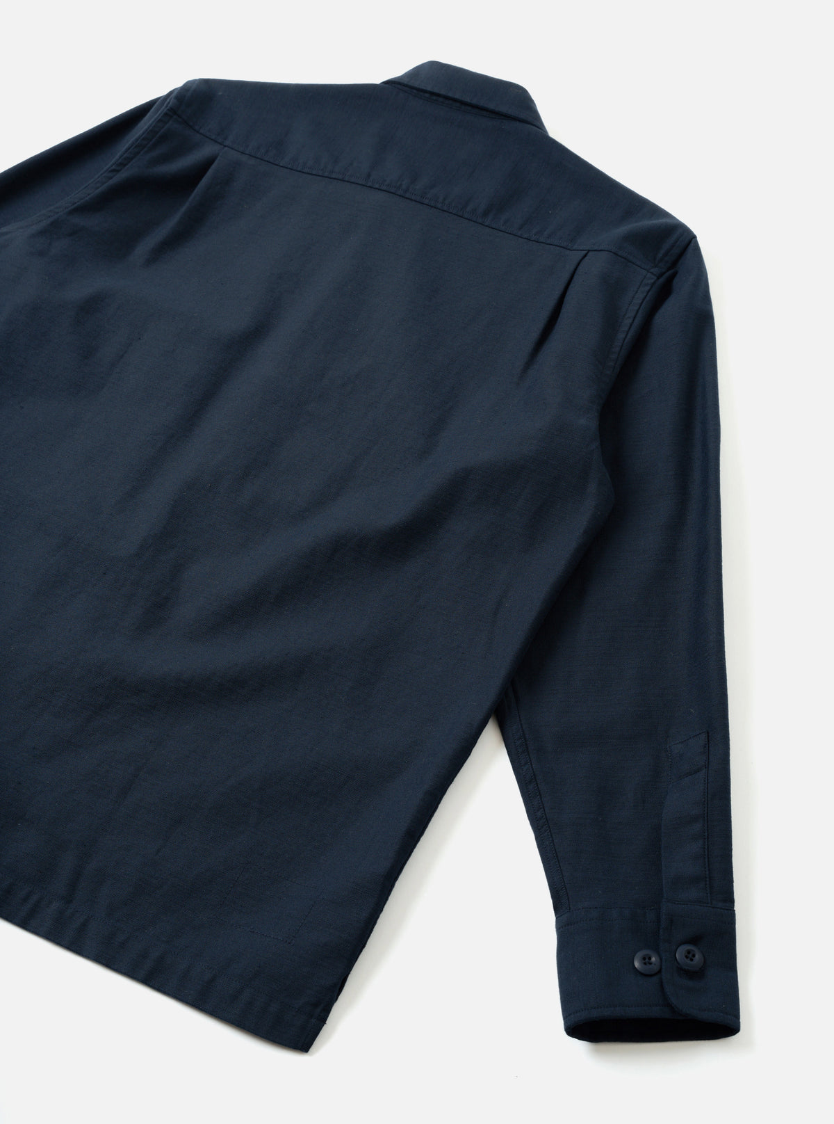 Back view of the Navy Slub Sateen Fatigue Shirt set against a plain off-white background. The image highlights the clean rear seams, straight hem, and subtle slub texture of the dark navy fabric.