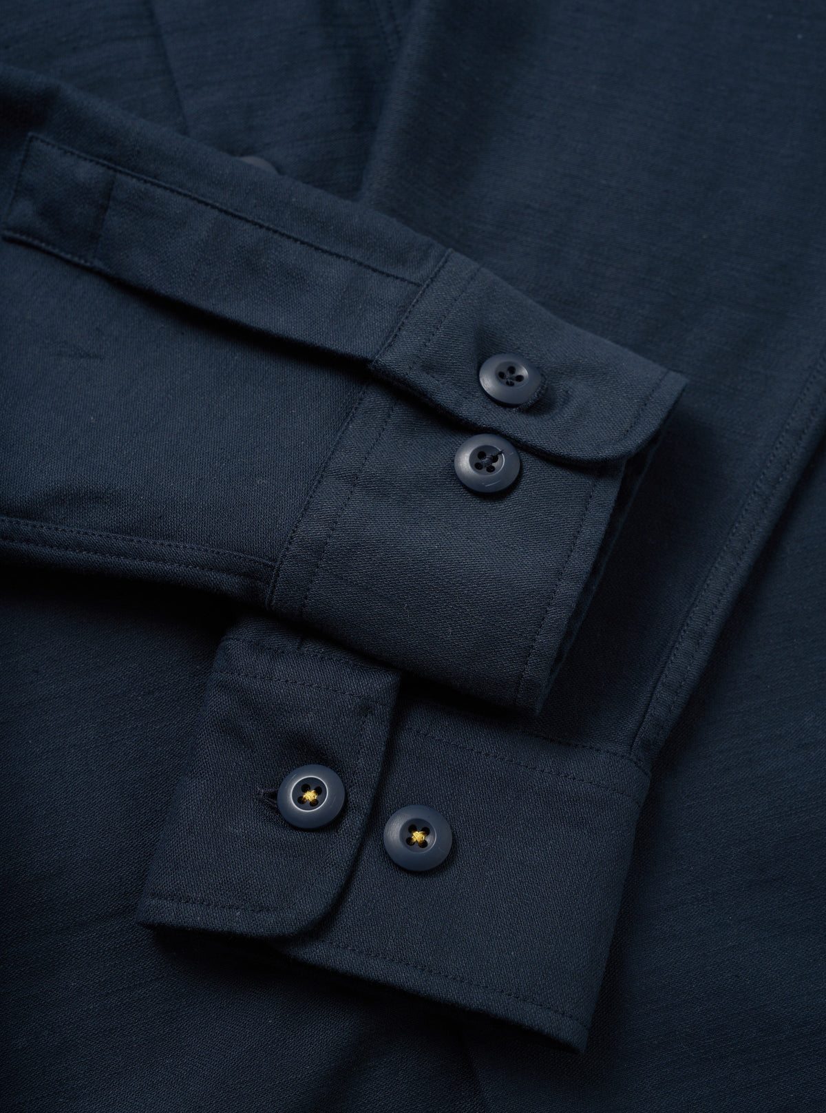 A side profile view of the Navy Slub Sateen Fatigue Shirt displayed against a white studio background. The image highlights the sleeve cuff details, side seam tailoring, and textured cotton fabric.