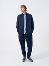 A male model wears the Navy Slub Sateen Fatigue Shirt unbuttoned over a top, posing against a neutral studio backdrop. The front view demonstrates the relaxed drape, chest pockets, and overall fit.