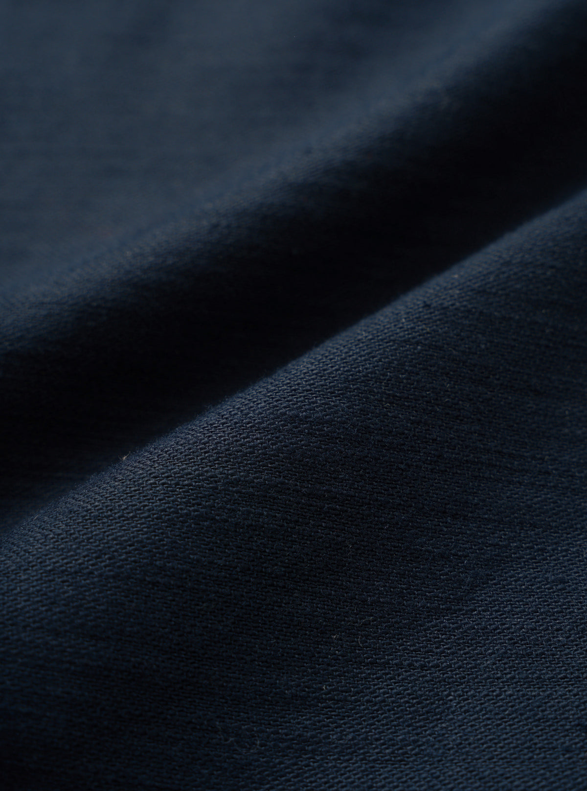 A close-up fabric swatch image showing the rich texture and fine weave of the Navy Slub Sateen Fatigue Shirt. The macro shot fills the frame to emphasize the dark navy cotton slub sateen material.