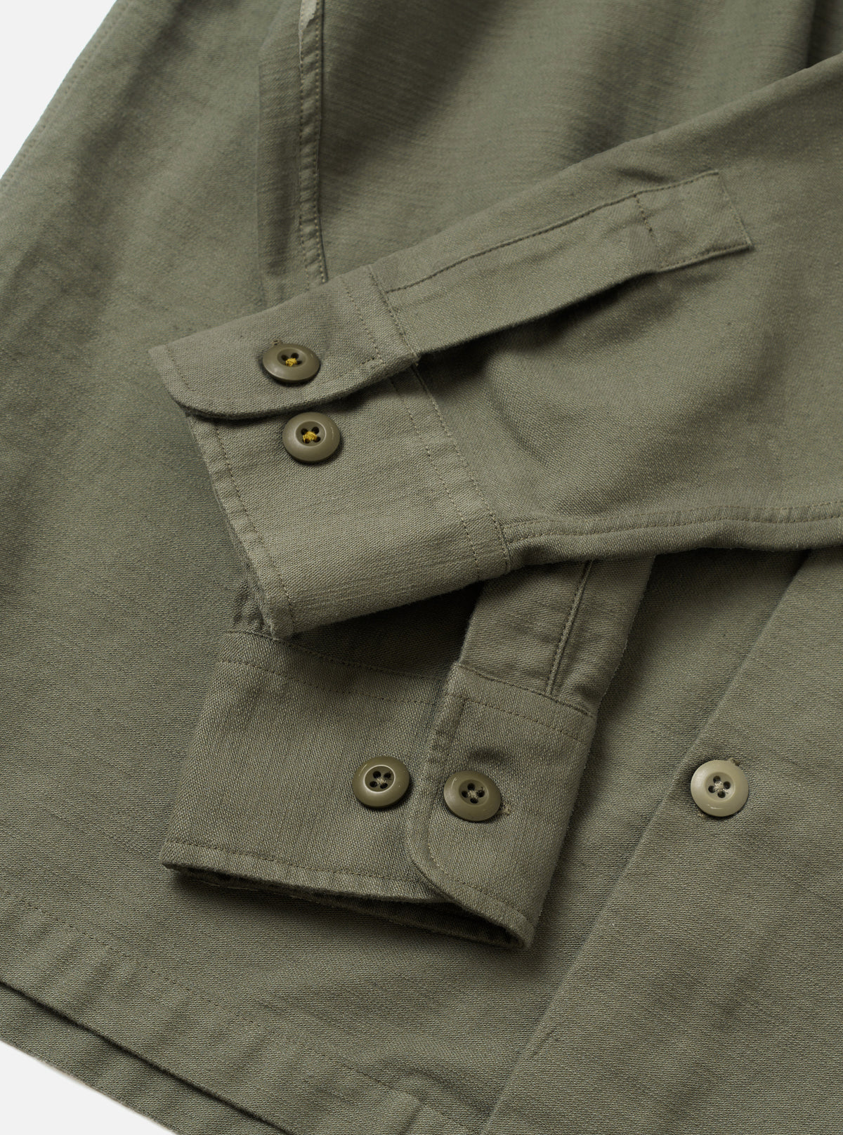 A side profile shot of the Olive Slub Sateen Fatigue Shirt displayed against a simple white backdrop. The view highlights the sleeve construction, cuff details, and relaxed fit of the olive overshirt.