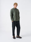 A male model wears the Olive Slub Sateen Fatigue Shirt in a front view shot against a neutral studio background. The photo showcases the olive green color, casual layering style, and chest pockets.