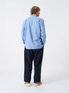 A male model poses in a studio setting wearing the Sky Blue Monty Cotton Tencel Standard Shirt unbuttoned over a plain top. The side-angled shot highlights the casual drape, chest pocket detail, and sleeve cuffs.
