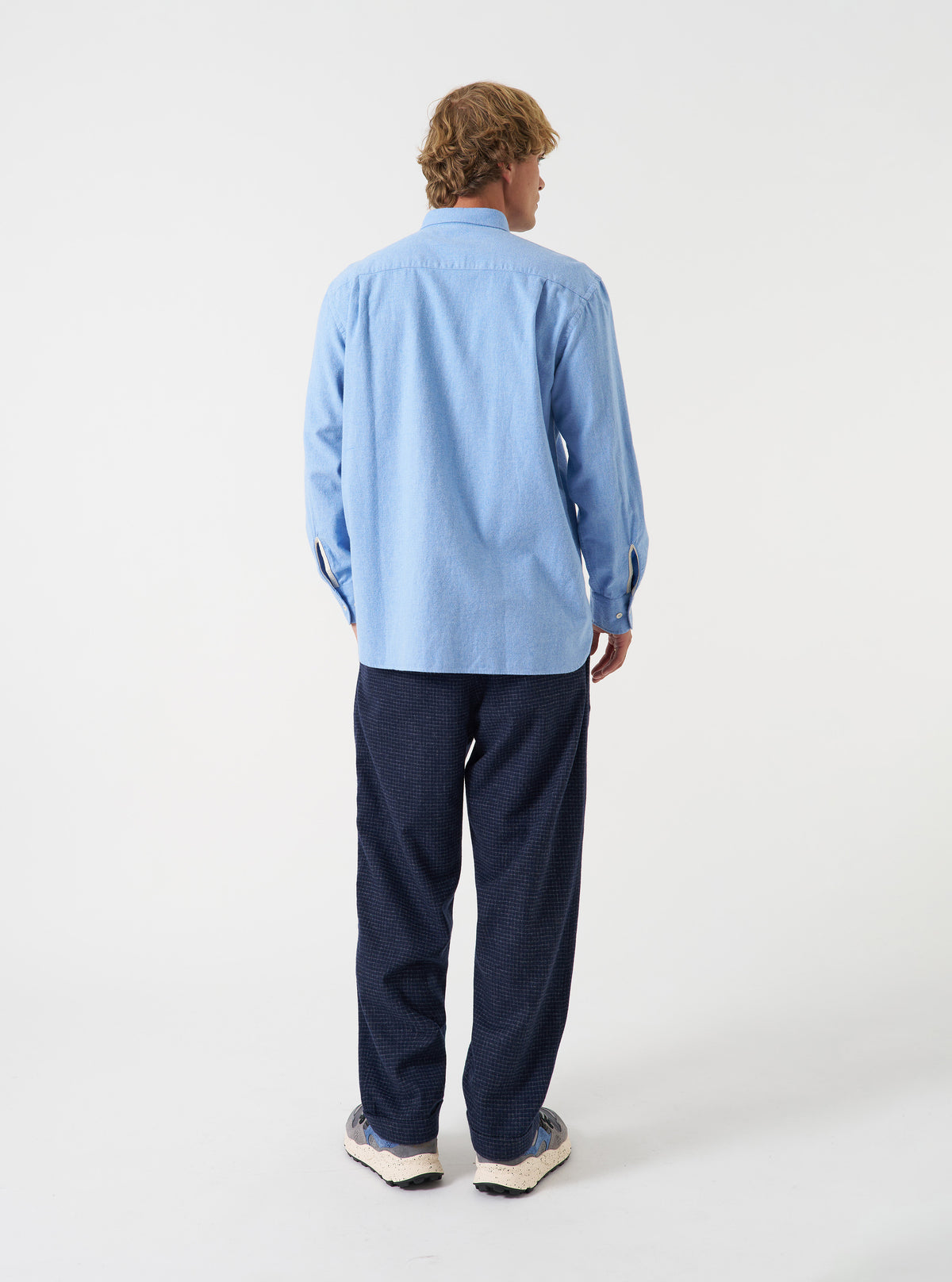 A male model poses against a neutral studio backdrop wearing the Blue Brushed Flannel Square Pocket Shirt. The angled view showcases the fit across the shoulders, sleeve construction, and soft flannel texture.