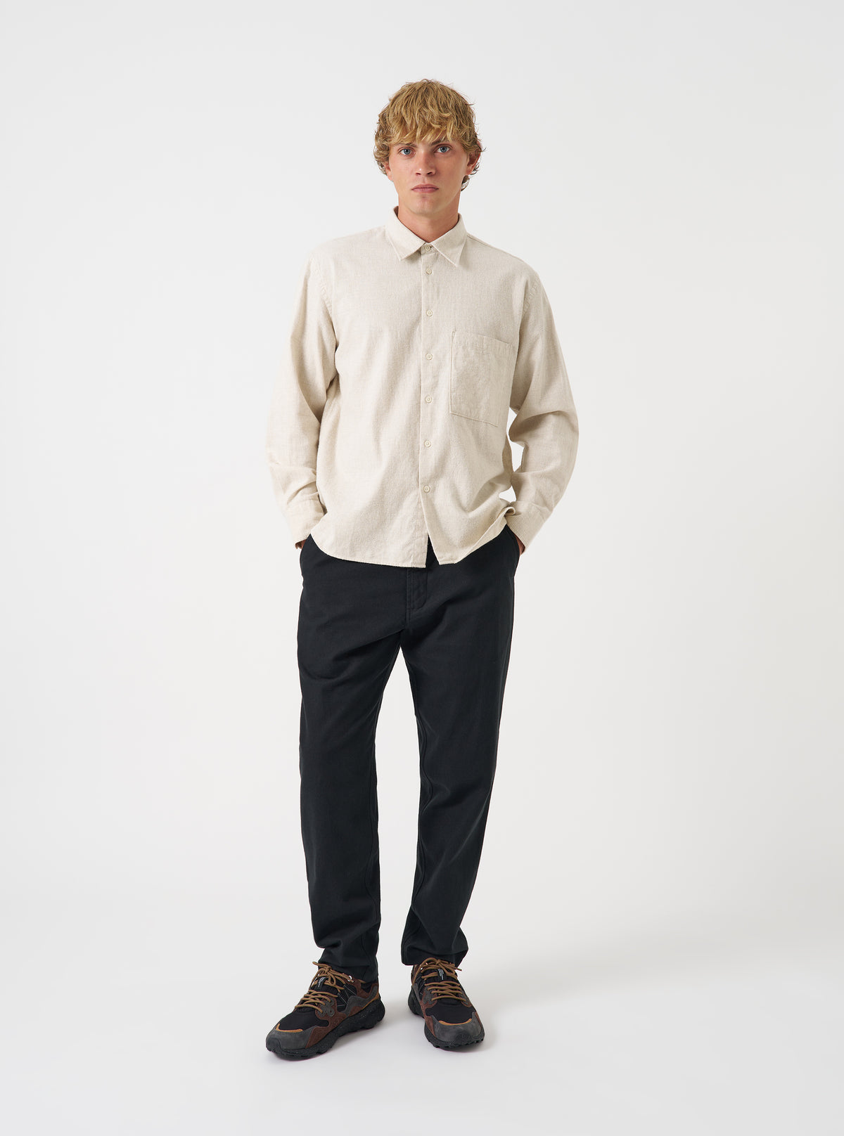 A male model wears the Ecru Brushed Flannel Square Pocket Shirt standing against a plain neutral background. The full front view highlights the light ecru tone, chest pockets, and button-up closure.