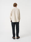 A male model poses in a neutral studio background wearing the Ecru Brushed Flannel Square Pocket Shirt. The three-quarter shot showcases the soft fabric texture, relaxed fit, and sleeve button details.