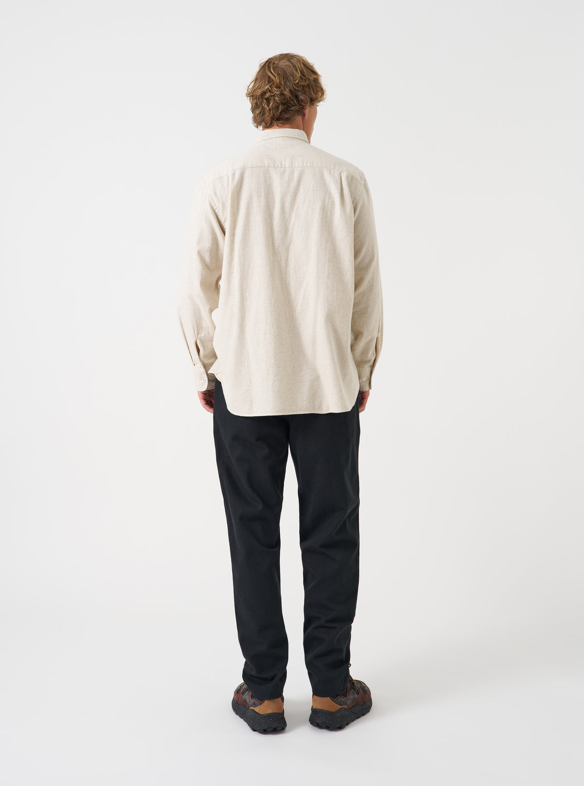 A male model poses in a neutral studio background wearing the Ecru Brushed Flannel Square Pocket Shirt. The three-quarter shot showcases the soft fabric texture, relaxed fit, and sleeve button details.