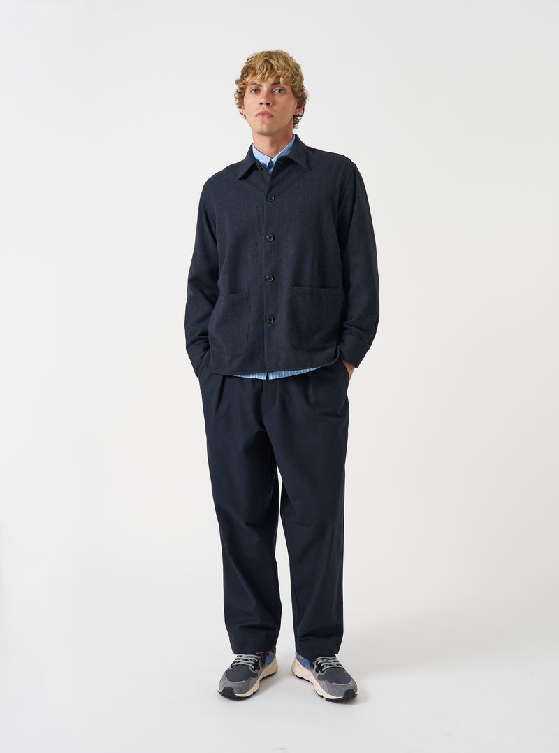 A male model stands against a studio backdrop wearing the Navy Airline Flannel Travail Overshirt buttoned up. The front shot highlights the pointed collar, spacious front pockets, and durable dark blue fabric.