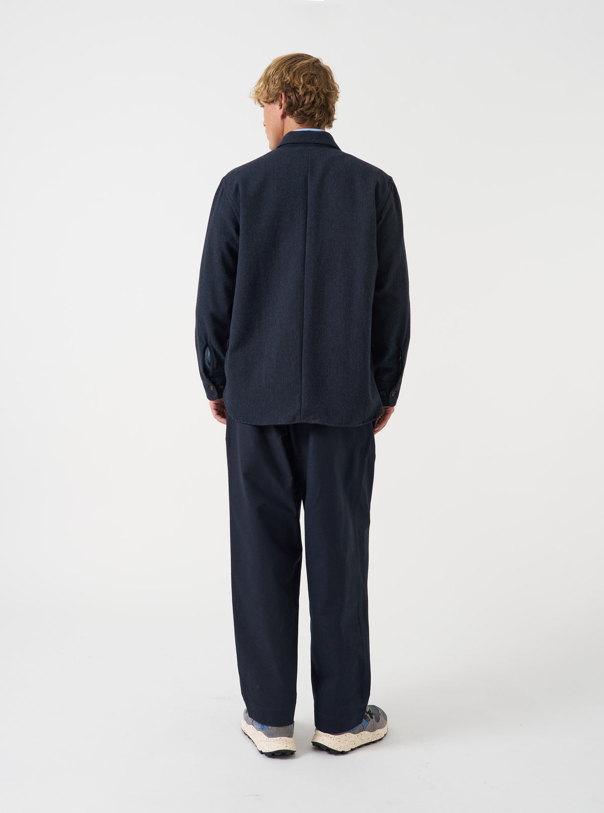 A male model wears the Navy Airline Flannel Travail Overshirt unbuttoned in a side-angled pose against a neutral background. The shot displays the relaxed layering fit, structured collar, and deep navy hue.