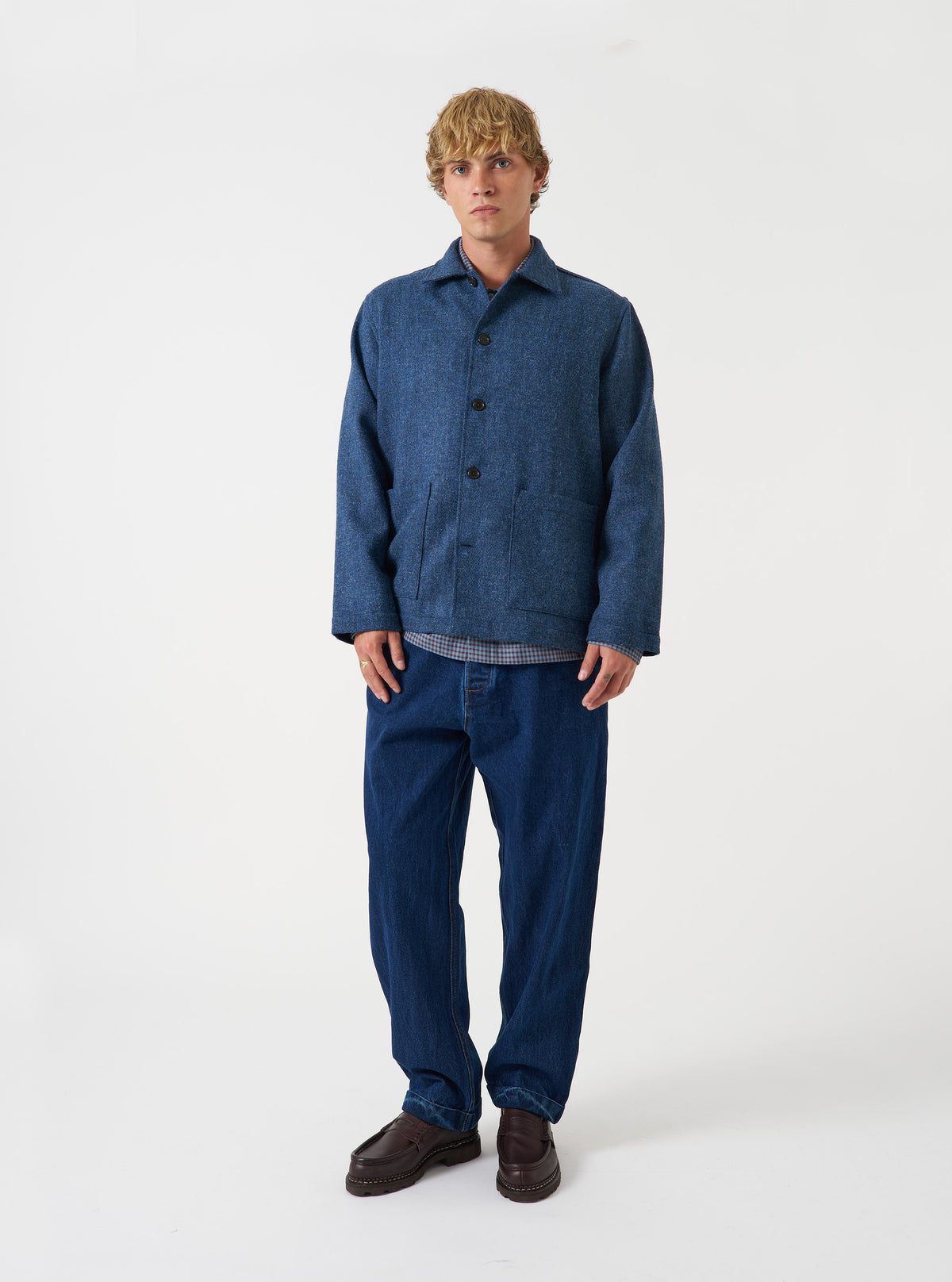 A male model wears the Blue Harris Tweed Easy Jacket buttoned up while standing against a neutral studio backdrop. The front shot highlights the jacket's structured fit, tailored lapels, and practical front pockets.