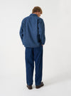 A male model poses against a plain studio background wearing the Blue Harris Tweed Easy Jacket open over a top. The three-quarter shot showcases the relaxed tailoring, sleeve construction, and rich textured wool.