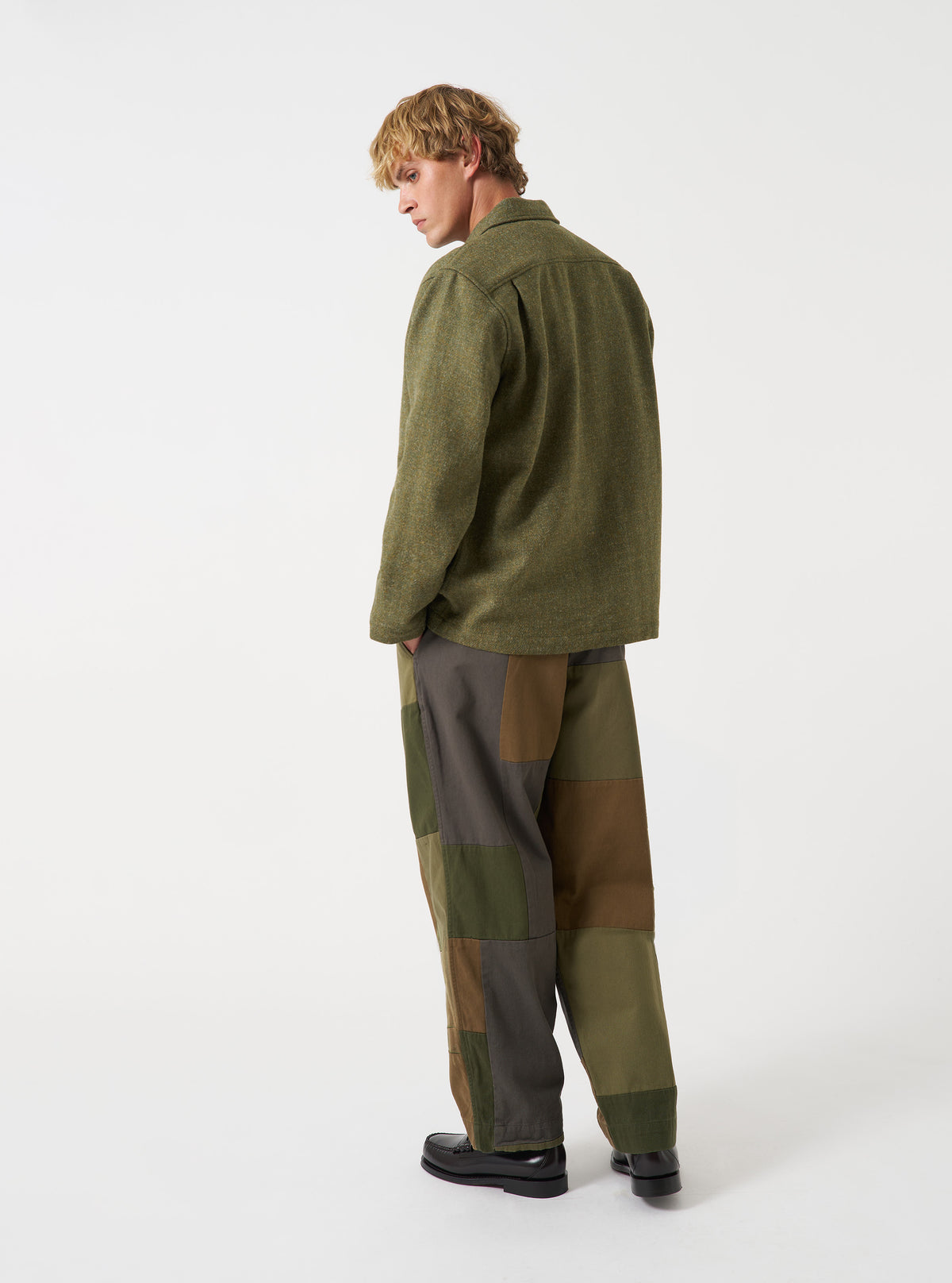 A male model poses wearing the Olive Harris Tweed Easy Jacket unbuttoned in a studio shot. The three-quarter view displays how the jacket drapes, showing inner lining details and pocket placement.