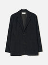 Black corduroy two-button jacket laid flat on a light grey studio backdrop. Notched lapels, open front, two large patch pockets at the hip, one chest patch pocket, dark horn-effect buttons, and full-length sleeves. A Universal Works woven label is visible at the collar. Fine cord texture throughout.